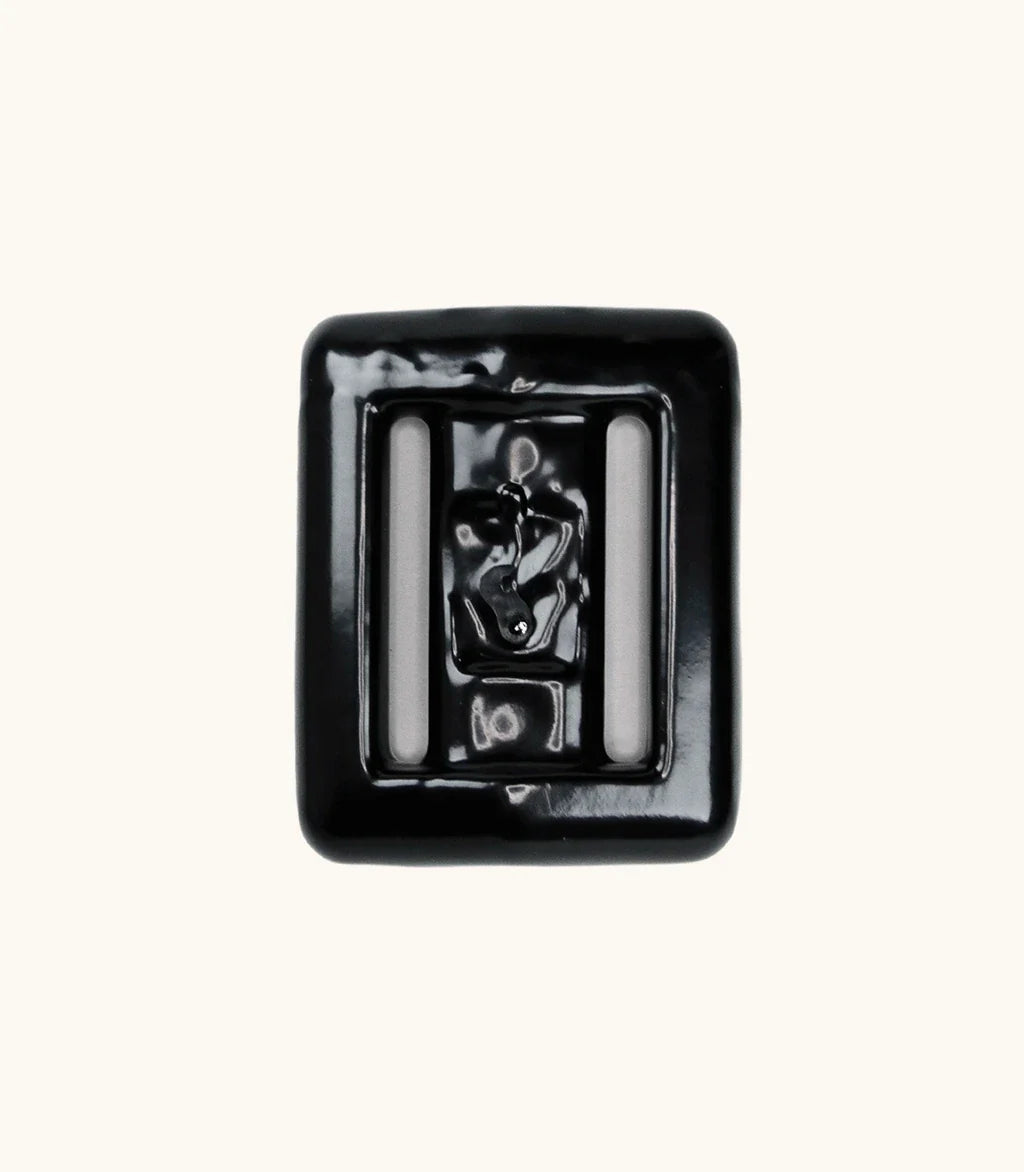 Close-up of a single black lava rock dive weight with glossy coating and two integrated belt slots, shown against a clean off-white background.