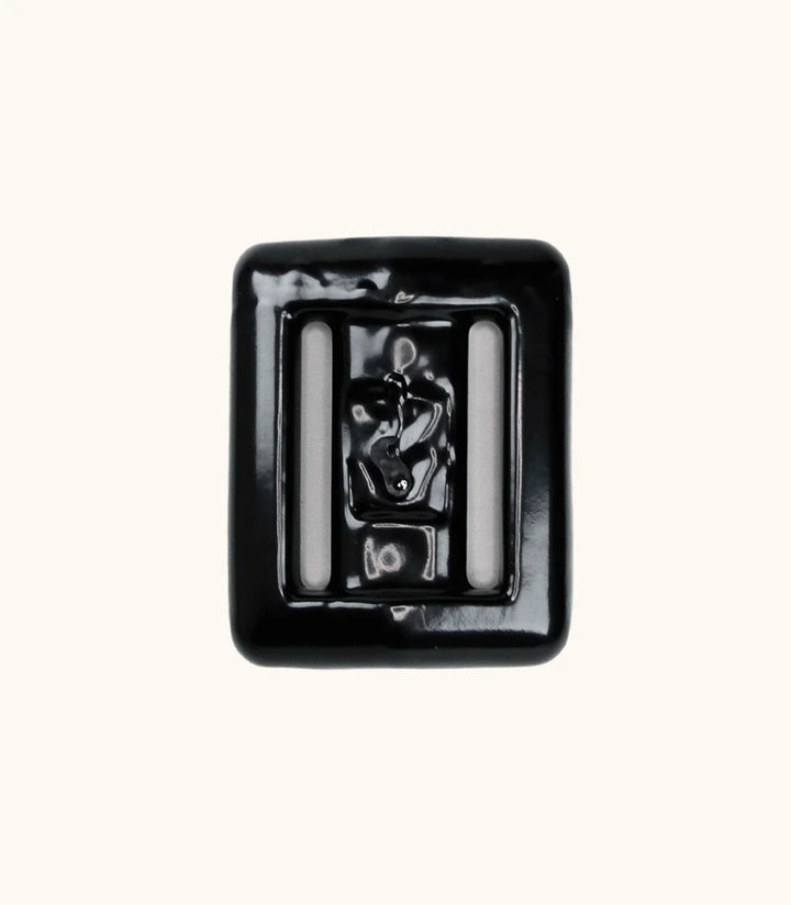 Close-up of a single black lava rock dive weight with glossy coating and two integrated belt slots, shown against a clean off-white background.