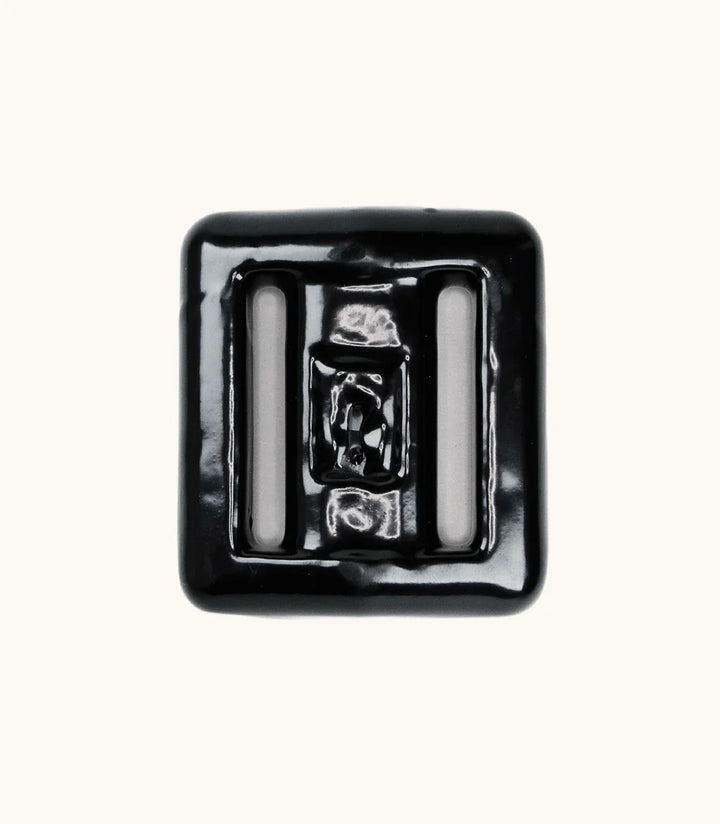 Black rubber-coated lava rock dive weight with two strap slots, photographed from above on a light background.